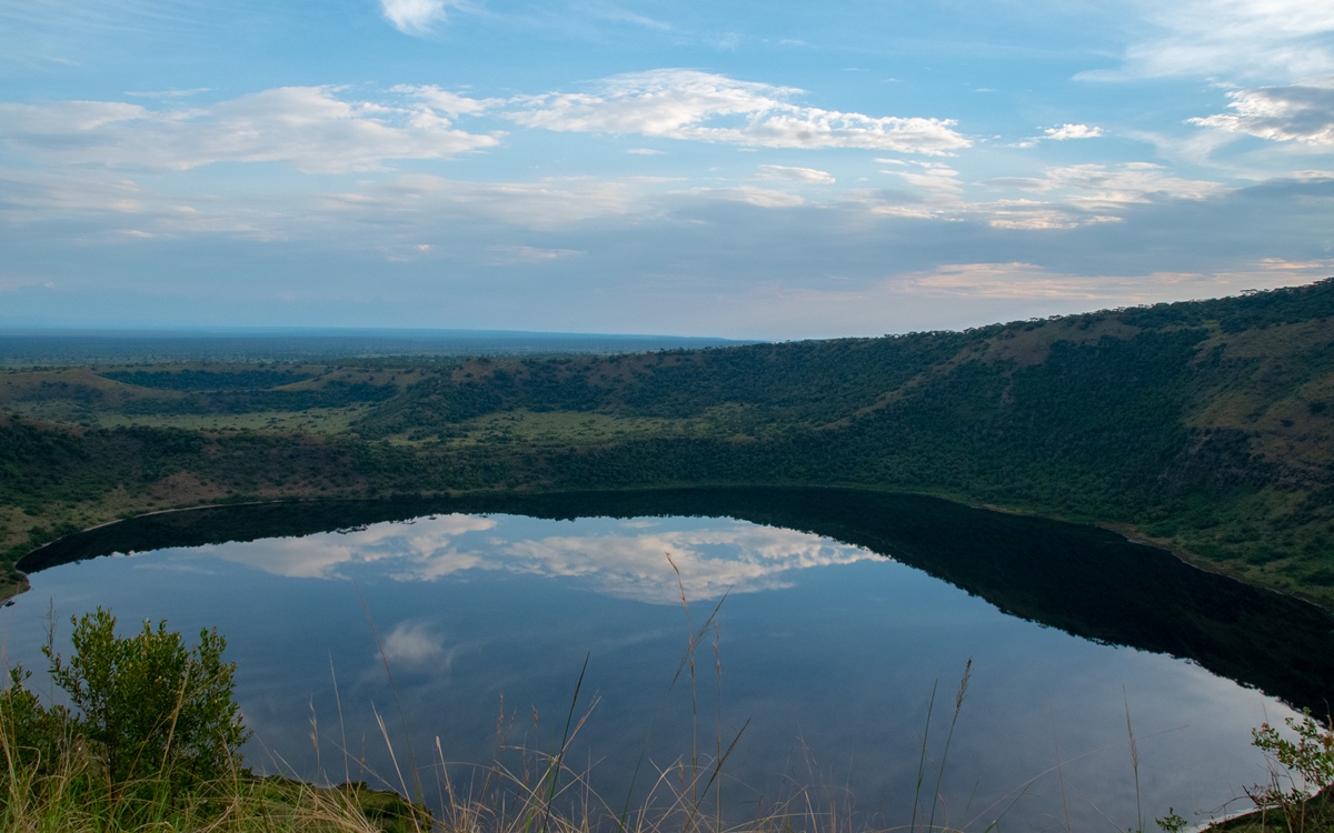 A photograph of the mountain ranges and a crater lake captured during the sunrise in Queen Elizabeth National Park in the Western Region of Uganda.