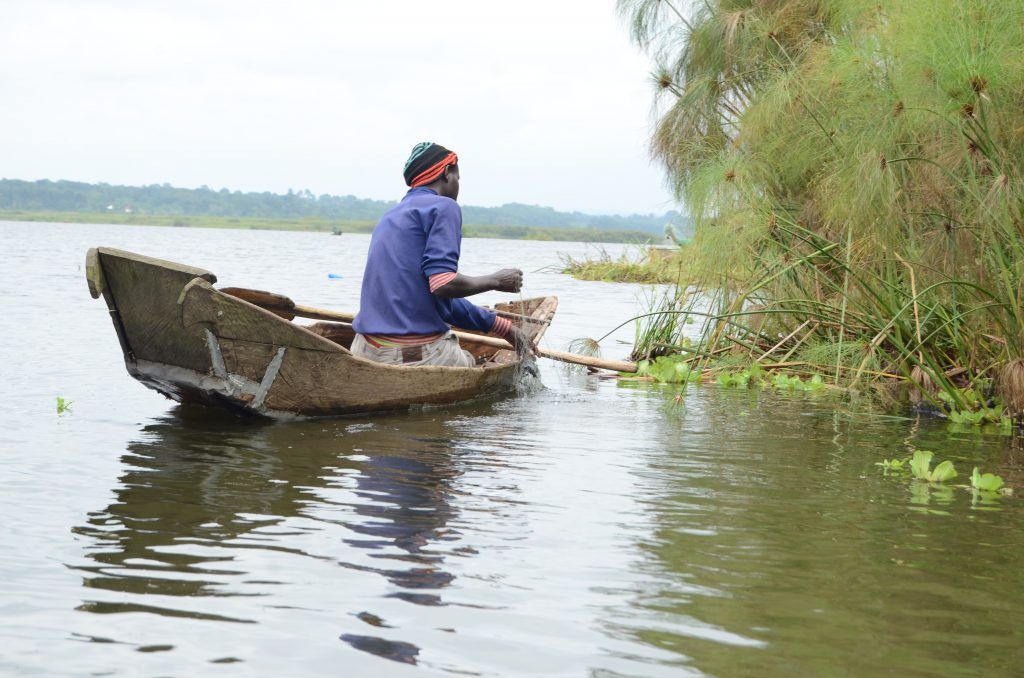 A photograph of fisherman in local boat canoe with a lake view in the background taken during a boat tour on Lake Wamala in Mityana in Central Uganda