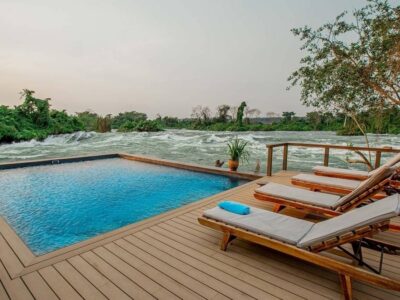 A photograph showing beach chairs, a swimming pool and the Mighty Nile River taken from Wildwaters Lodge in Uganda.