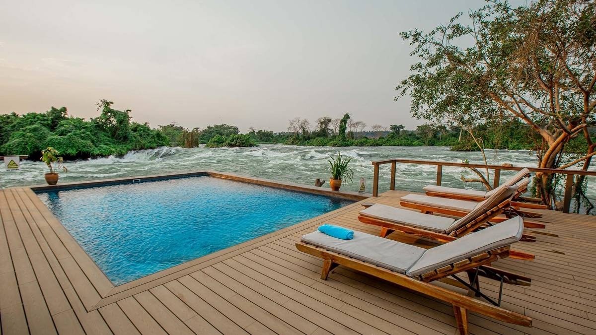 A photograph showing beach chairs, a swimming pool and the Mighty Nile River taken from Wildwaters Lodge in Uganda.