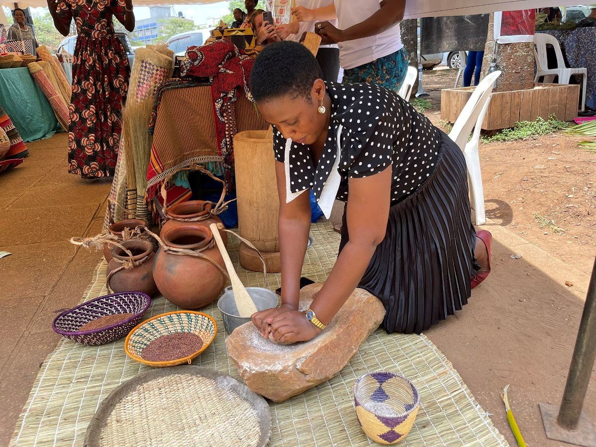 A photograph of a woman illustrating the grinding process taken during a Cultural Show at the Uganda National Cultural Centre in Kampala, Uganda.