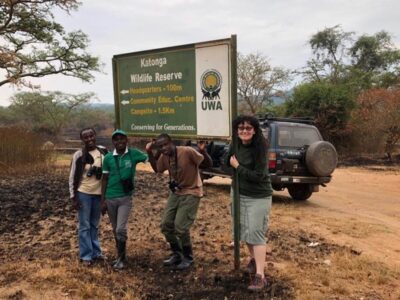 A photograph of tourists posing at the Katonga Wildlife Reserve signpost, Western Uganda