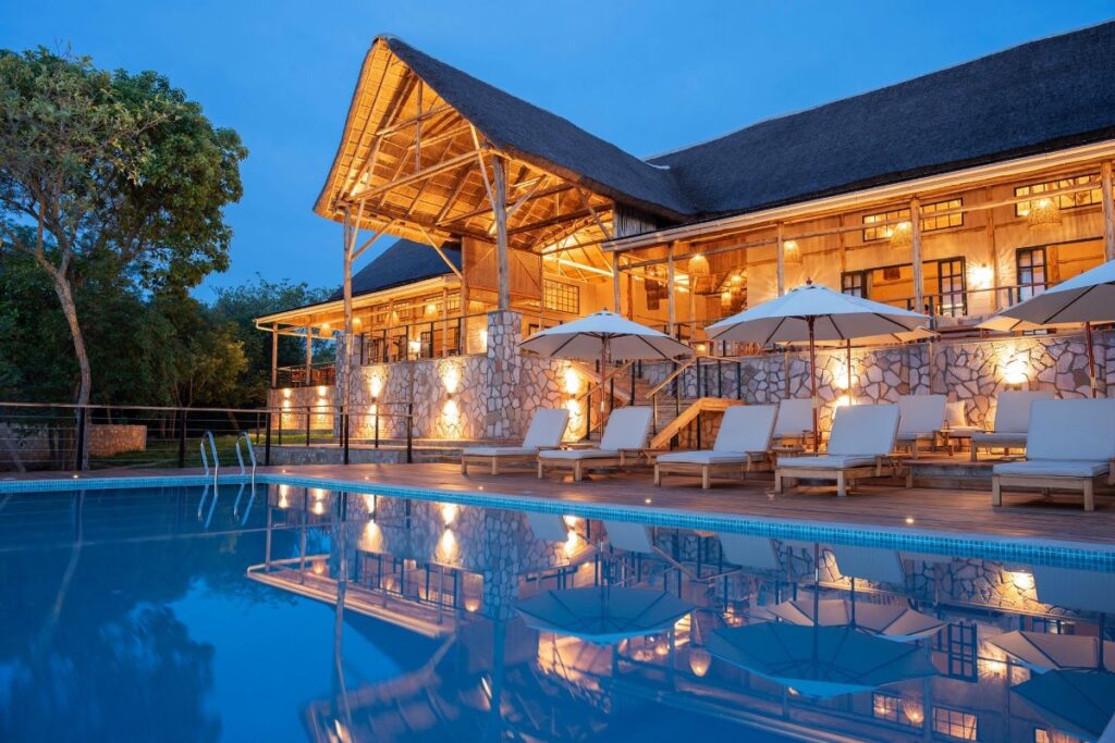 Stunning evening glow at Pabidi Lodge’s swimming pool, reflecting the elegant thatched-roof main lodge nestled in the forest