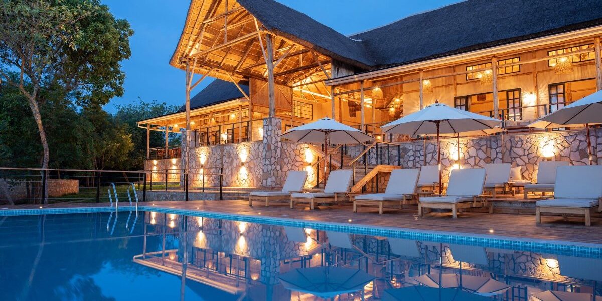Stunning evening glow at Pabidi Lodge’s swimming pool, reflecting the elegant thatched-roof main lodge nestled in the forest