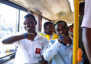 Smiling students proudly display their tap-to-pay wristbands inside one of the new electric buses, enjoying safe, convenient, and cashless transport to and from school