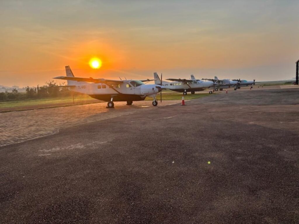 A row of Kampala Executive Aviation Cessna aircraft, including the Cessna 208 Caravan, lined up on the airfield at sunset, ready for scenic flights over Lake Victoria and the Entebbe peninsula