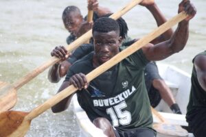 The Busujju crew powers through the water in a canoe marked with Bunjako Beach and Coronation Regatta branding during competitive racing at the event
