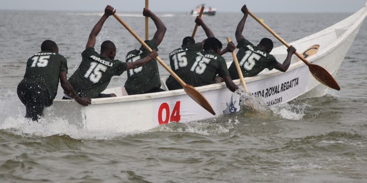 Competitors from the Buweekula team paddle vigorously in a traditional canoe during the Buganda Royal Regatta at Bunjako Beach, sending up sprays of water as they race across the lake