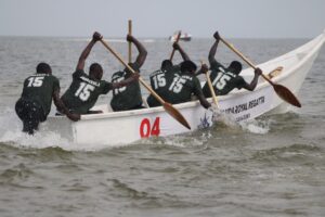 Competitors from the Buweekula team paddle vigorously in a traditional canoe during the Buganda Royal Regatta at Bunjako Beach, sending up sprays of water as they race across the lake
