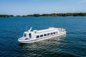 The passenger vessel MV Vanessa carries travelers across open water, with a tree-lined shoreline visible in the background under clear skies