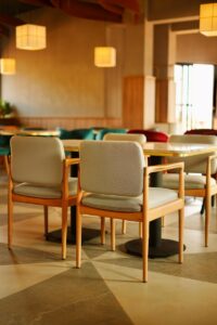 Dining tables with marble tops and light-wood armchairs in the main seating area of Café Shires, set against a geometric tiled floor and soft pendant lighting