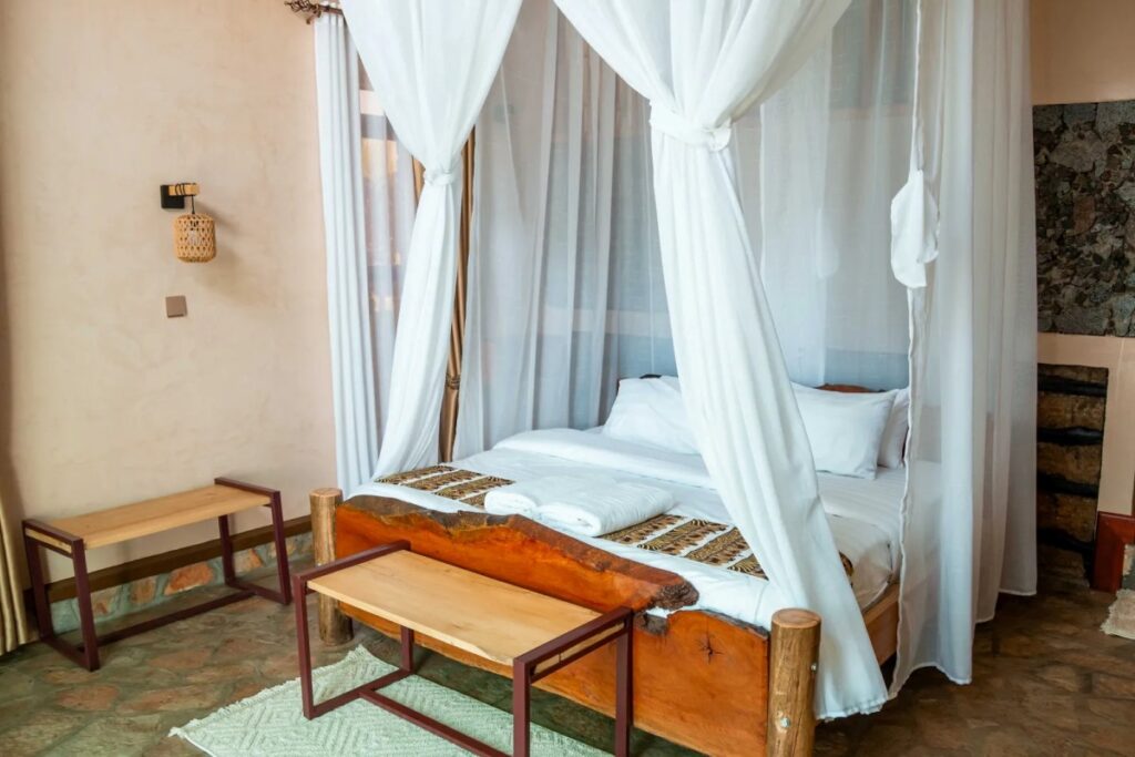 Bright and airy villa interior at Rift Craters Eco Lodge, showcasing natural stone flooring, wooden furniture, and floor-to-ceiling mosquito netting that opens toward the surrounding landscape