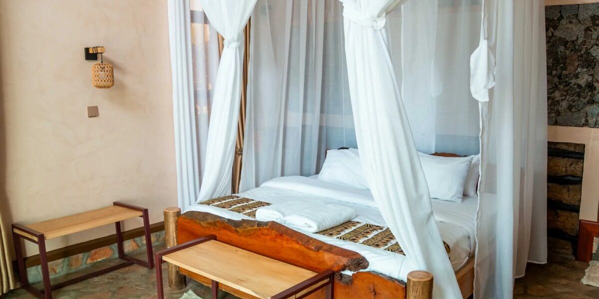 Bright and airy villa interior at Rift Craters Eco Lodge, showcasing natural stone flooring, wooden furniture, and floor-to-ceiling mosquito netting that opens toward the surrounding landscape