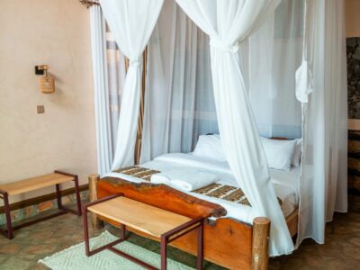 Bright and airy villa interior at Rift Craters Eco Lodge, showcasing natural stone flooring, wooden furniture, and floor-to-ceiling mosquito netting that opens toward the surrounding landscape