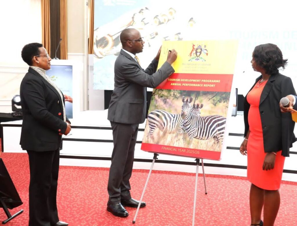 Finance Minister Hon. Henry Musasizi signs the Tourism Development Programme Annual Performance Report for Financial Year 2025/26 during the official unveiling at the 4th Annual Tourism Development Programme Review Conference, Imperial Royale Hotel, Kampala